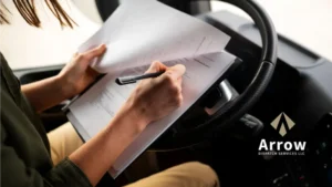 A truck driver reviewing and signing dispatch paperwork inside the cab, representing Arrow Dispatch Services LLC’s professional trucking support.