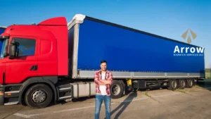 A smiling truck driver stands confidently in front of a large red and blue semi-truck with the Arrow Dispatch Services LLC logo displayed on the trailer.